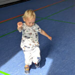 Ein kleines Kind läuft in der Turnhalle auf einen Ball zu.