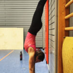 Ein Mädchen macht Handstand an einer Wand in der Turnhalle.