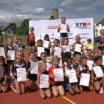 Turnerinnen stehen auf und neben einem Podest des Schwäbischen Turnerbunds und halten die Urkunden in der Hand. Das Podest ist in Kastenform auf einem Sportplatz aufgebaut. (Foto: Jörg Allmendinger)