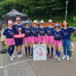 Mannschaftsaufnahme zum Kleinspielfeldturnier 2024 von sieben Frauen und einem Mann, die ihre Sportoutfits mit Sonnenschutz und Sonnenbrille tragen. Der Mann trägt einen Falmingo-Schwimmreifen.