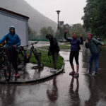 Vier Personen stehen in Regenkleidung neben ihren Fahrrädern und machen teils lustige Posen.