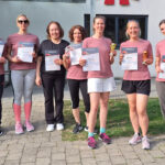 Sieben Frauen und ein Kind halten Urkunden vom Tischtennisturnier 2025 vor der Turnhalle Aistaig in die Kamera.