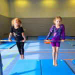 Zwei Mädchen in Turnkleidung stützen sich auf einer Rechstange.