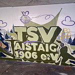 Das Bild zeigt ein Graffiti mit dem Schriftzug "TSV Aistaig 1906 e.V.", ergänzt durch Bienen, Wolken und eine Landschaft. Der Hintergrund ist mit grünen und blauen Farbtönen gestaltet.